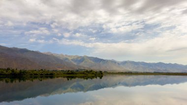 Yeşil vadiler ve görkemli dağlarla çevrili sessiz bir dağ gölü Issyk-Kul. Kırgızistan 'da turizm ve huzurlu dinlenme için mükemmel bir yer.