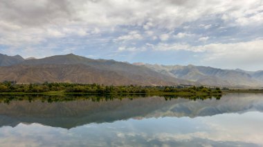 Yeşil vadiler ve görkemli dağlarla çevrili sessiz bir dağ gölü Issyk-Kul. Kırgızistan 'da turizm ve huzurlu dinlenme için mükemmel bir yer.