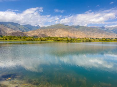 Yeşil vadiler ve görkemli dağlarla çevrili sessiz bir dağ gölü Issyk-Kul. Kırgızistan 'da turizm ve huzurlu dinlenme için mükemmel bir yer.