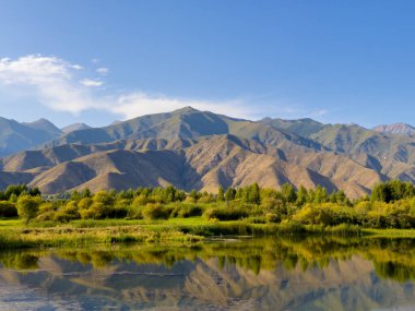 Yeşil vadiler ve görkemli dağlarla çevrili sessiz bir dağ gölü Issyk-Kul. Kırgızistan 'da turizm ve huzurlu dinlenme için mükemmel bir yer.