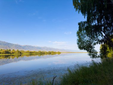 Yeşil vadiler ve görkemli dağlarla çevrili sessiz bir dağ gölü Issyk-Kul. Kırgızistan 'da turizm ve huzurlu dinlenme için mükemmel bir yer.