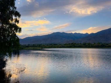 Yeşil vadiler ve görkemli dağlarla çevrili sessiz bir dağ gölü Issyk-Kul. Kırgızistan 'da turizm ve huzurlu dinlenme için mükemmel bir yer.