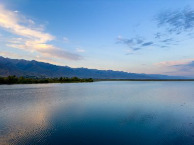 Arka planda görkemli dağlarla Issyk-Kul gölünün sakin su yüzeyi. Kırgızistan 'ın güzel doğal manzarası.