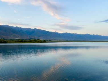 Sessiz dağ gölü, akşam güneşi, Kırgızistan. Gölde durgun su ve dağ yansıması.