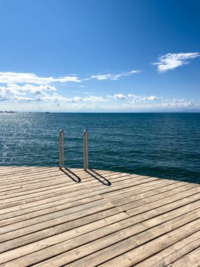 Gölün berrak sularına giden metal bir merdiveni olan tahta bir güverte. Bulutsuz bir gökyüzü ile güneşli bir gün.