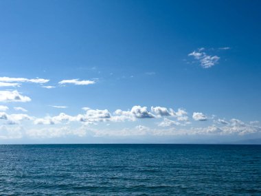 Issyk-Kul Gölü 'nün arka planında bulutlu bir gökyüzü ve dağlar var. Su sakin, gökyüzünü yansıtıyor. Sabahın erken saatlerinde doğanın dinginliği ve huzuru