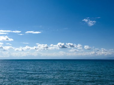 Issyk-Kul Gölü 'nün arka planında bulutlu bir gökyüzü ve dağlar var. Su sakin, gökyüzünü yansıtıyor. Sabahın erken saatlerinde doğanın dinginliği ve huzuru