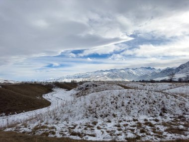 Kırgızistan 'da dağları kaplayan kar bulutlu kış gökyüzü altında huzurlu kırsal alan.