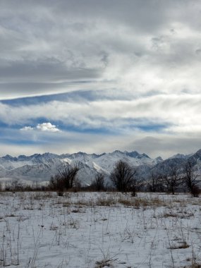 Kırgızistan 'da dağları kaplayan kar bulutlu kış gökyüzü altında huzurlu kırsal alan.