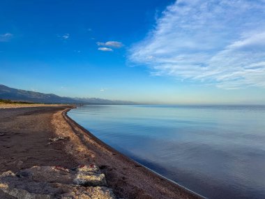 Sessiz dağ gölü, akşam güneşi, Kırgızistan. Gölde durgun su ve dağ yansıması var. Issyk-Kul 'un üzerinde gün batımı sakin sulardaki yansımalarla