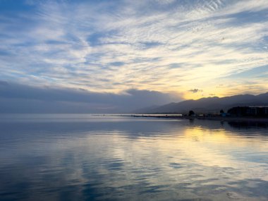 Sessiz dağ gölü, akşam güneşi, Kırgızistan. Gölde durgun su ve dağ yansıması var. Issyk-Kul 'un üzerinde gün batımı sakin sulardaki yansımalarla