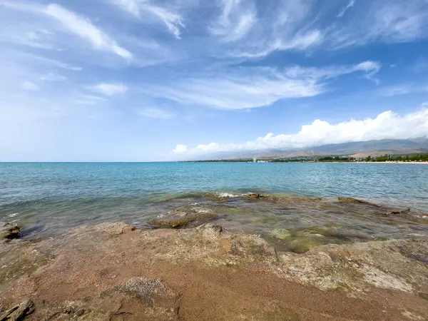 Uçsuz bucaksız gökyüzünün altında Issyk-Kul 'un kayalık kıyısı ve berrak suyu.