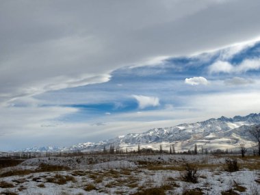 Kırgızistan 'da dağları kaplayan kar bulutlu kış gökyüzü altında huzurlu kırsal alan.