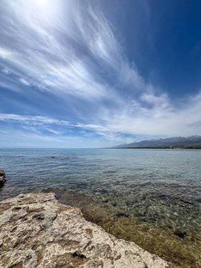 Uçsuz bucaksız gökyüzünün altında Issyk-Kul 'un kayalık kıyısı ve berrak suyu.