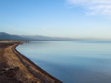 Sessiz dağ gölü, akşam güneşi, Kırgızistan. Gölde durgun su ve dağ yansıması var. Issyk-Kul 'un üzerinde gün batımı sakin sulardaki yansımalarla