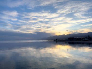 Sessiz dağ gölü, akşam güneşi, Kırgızistan. Gölde durgun su ve dağ yansıması var. Issyk-Kul 'un üzerinde gün batımı sakin sulardaki yansımalarla