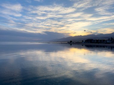 Sessiz dağ gölü, akşam güneşi, Kırgızistan. Gölde durgun su ve dağ yansıması var. Issyk-Kul 'un üzerinde gün batımı sakin sulardaki yansımalarla