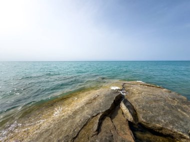 Uçsuz bucaksız gökyüzünün altında Issyk-Kul 'un kayalık kıyısı ve berrak suyu.