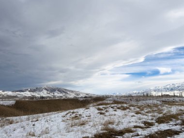 Kırgızistan 'da dağları kaplayan kar bulutlu kış gökyüzü altında huzurlu kırsal alan.