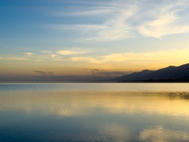 Sessiz dağ gölü, akşam güneşi, Kırgızistan. Gölde durgun su ve dağ yansıması