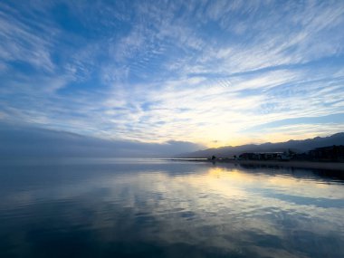 Sessiz dağ gölü, akşam güneşi, Kırgızistan. Gölde durgun su ve dağ yansıması var. Issyk-Kul 'un üzerinde gün batımı sakin sulardaki yansımalarla