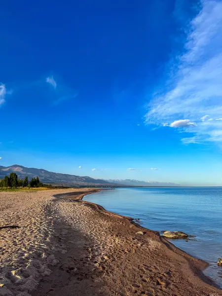 Sessiz dağ gölü, akşam güneşi, Kırgızistan. Gölde durgun su ve dağ yansıması var. Issyk-Kul 'un üzerinde gün batımı sakin sulardaki yansımalarla