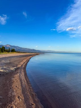 Sessiz dağ gölü, akşam güneşi, Kırgızistan. Gölde durgun su ve dağ yansıması var. Issyk-Kul 'un üzerinde gün batımı sakin sulardaki yansımalarla
