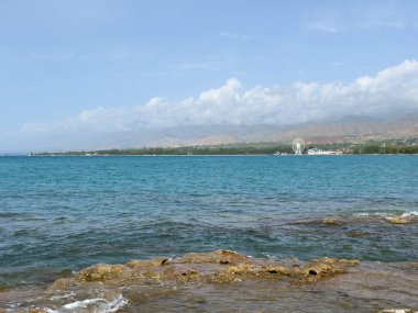 Uçsuz bucaksız gökyüzünün altında Issyk-Kul 'un kayalık kıyısı ve berrak suyu.