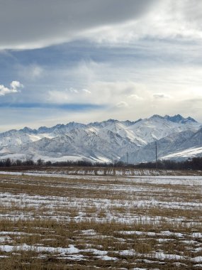 Kırgızistan 'da dağları kaplayan kar bulutlu kış gökyüzü altında huzurlu kırsal alan.