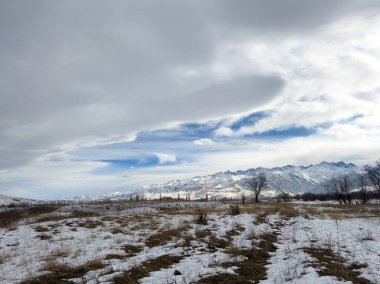 Kırgızistan 'da dağları kaplayan kar bulutlu kış gökyüzü altında huzurlu kırsal alan.