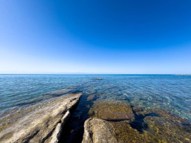 Uçsuz bucaksız gökyüzünün altında Issyk-Kul 'un kayalık kıyısı ve berrak suyu.