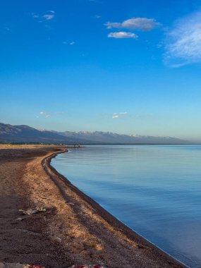 Sessiz dağ gölü, akşam güneşi, Kırgızistan. Gölde durgun su ve dağ yansıması var. Issyk-Kul 'un üzerinde gün batımı sakin sulardaki yansımalarla