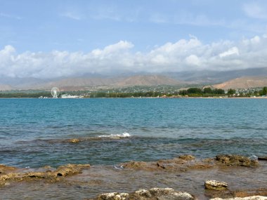 Uçsuz bucaksız gökyüzünün altında Issyk-Kul 'un kayalık kıyısı ve berrak suyu.