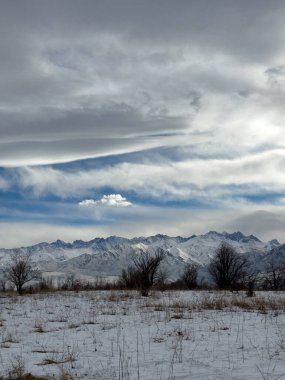 Kırgızistan 'da dağları kaplayan kar bulutlu kış gökyüzü altında huzurlu kırsal alan.