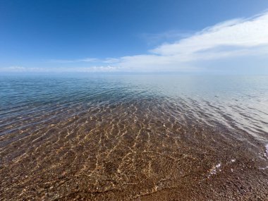 Temiz göl suyu ve çakıl taşı tabanı güneş yansımaları altında.