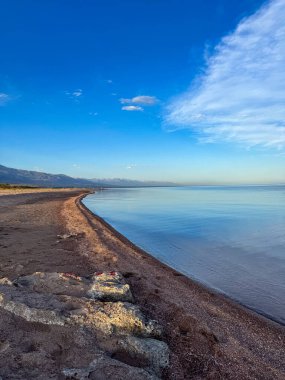 Sessiz dağ gölü, akşam güneşi, Kırgızistan. Gölde durgun su ve dağ yansıması var. Issyk-Kul 'un üzerinde gün batımı sakin sulardaki yansımalarla