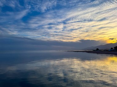 Sessiz dağ gölü, akşam güneşi, Kırgızistan. Gölde durgun su ve dağ yansıması var. Issyk-Kul 'un üzerinde gün batımı sakin sulardaki yansımalarla