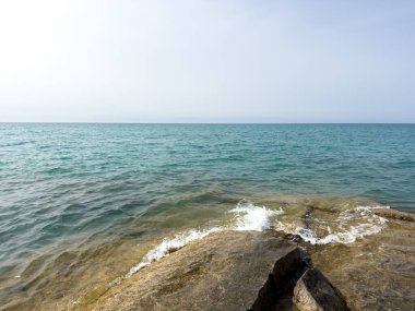Uçsuz bucaksız gökyüzünün altında Issyk-Kul 'un kayalık kıyısı ve berrak suyu.