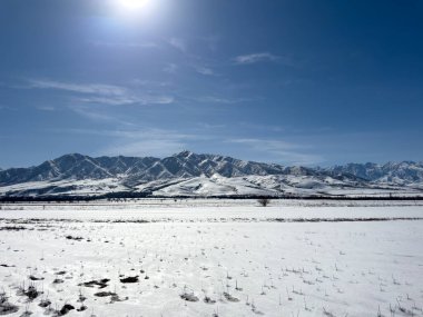 Kırgızistan 'da uzak sıradağları olan geniş karlı bir vadi. Parlak güneş ışığı ve derin mavi gökyüzü kış tarlaları üzerinde