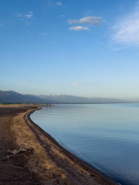 Sessiz dağ gölü, akşam güneşi, Kırgızistan. Gölde durgun su ve dağ yansıması var. Issyk-Kul 'un üzerinde gün batımı sakin sulardaki yansımalarla
