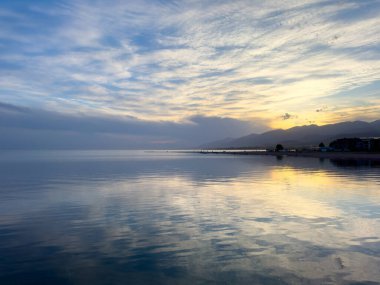 Sessiz dağ gölü, akşam güneşi, Kırgızistan. Gölde durgun su ve dağ yansıması var. Issyk-Kul 'un üzerinde gün batımı sakin sulardaki yansımalarla