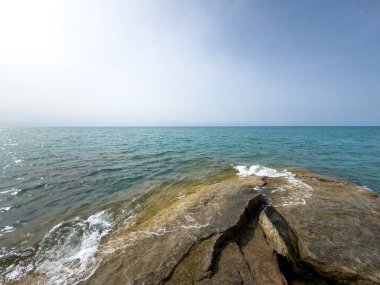 Uçsuz bucaksız gökyüzünün altında Issyk-Kul 'un kayalık kıyısı ve berrak suyu.