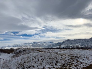 Kırgızistan 'da dağları kaplayan kar bulutlu kış gökyüzü altında huzurlu kırsal alan.