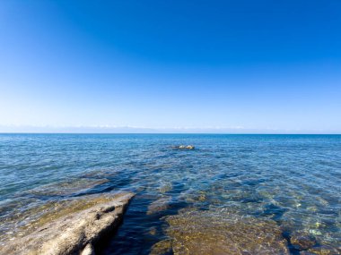 Uçsuz bucaksız gökyüzünün altında Issyk-Kul 'un kayalık kıyısı ve berrak suyu.