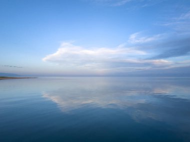Akşam sakin ve pürüzsüz göl yüzeyinde yumuşak bulutların altında.