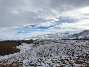 Kırgızistan 'da dağları kaplayan kar bulutlu kış gökyüzü altında huzurlu kırsal alan.