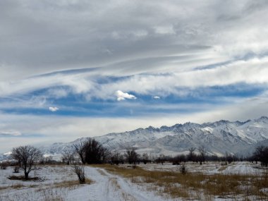 Kırgızistan 'da dağları kaplayan kar bulutlu kış gökyüzü altında huzurlu kırsal alan.