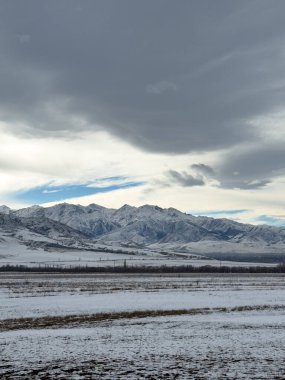 Kırgızistan 'da dağları kaplayan kar bulutlu kış gökyüzü altında huzurlu kırsal alan.