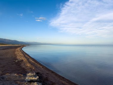 Sessiz dağ gölü, akşam güneşi, Kırgızistan. Gölde durgun su ve dağ yansıması var. Issyk-Kul 'un üzerinde gün batımı sakin sulardaki yansımalarla