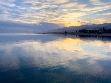 Sessiz dağ gölü, akşam güneşi, Kırgızistan. Gölde durgun su ve dağ yansıması var. Issyk-Kul 'un üzerinde gün batımı sakin sulardaki yansımalarla